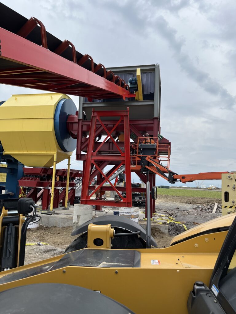 Red primary feed conveyor delivering material into an enclosed processing structure as part of the debris plant material flow.