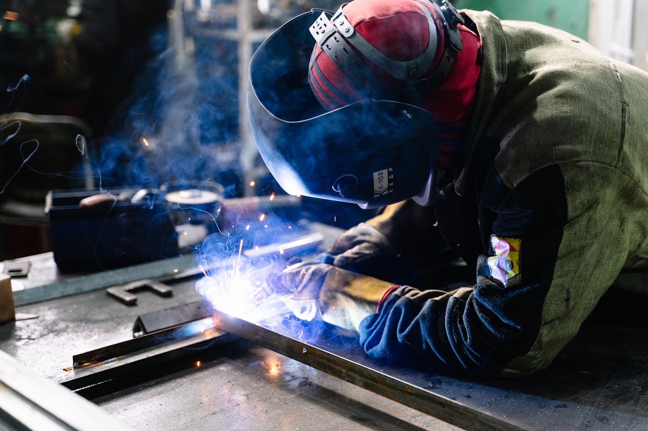 our-story A welder works on metal fabrication indoors, creating bright sparks and smoke.